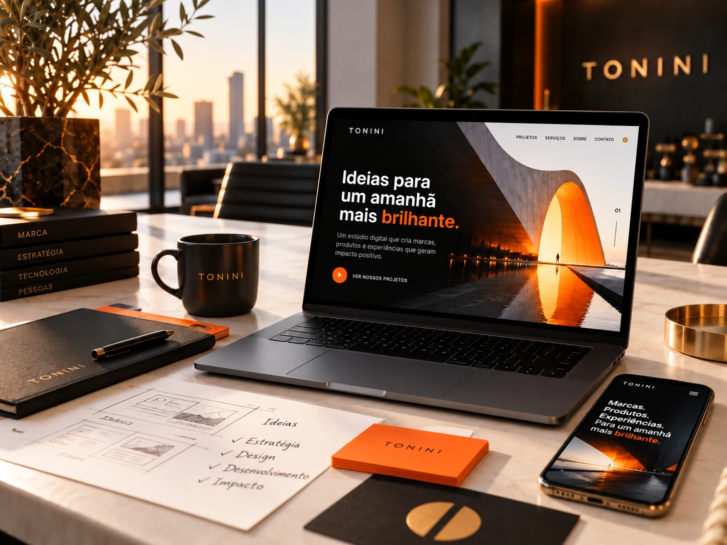 Ambiente criativo TONINI com notebook, celular e materiais da marca, em preto, laranja e dourado